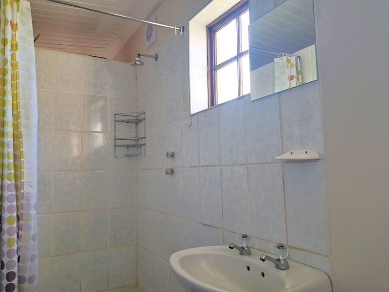 A functional bathroom featuring a wall-mounted basin, shower area with tiled walls, and a window for natural light.