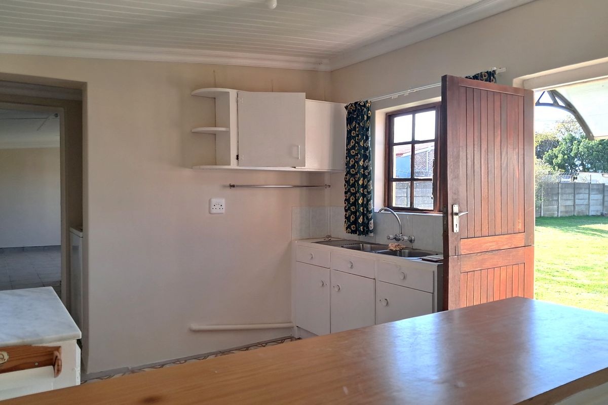 A functional kitchen area featuring built-in cabinetry, a stainless steel sink, and direct access to the garden through a timber door.