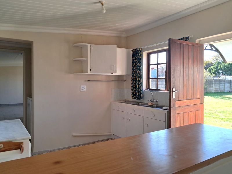 A functional kitchen area featuring built-in cabinetry, a stainless steel sink, and direct access to the garden through a timber door.