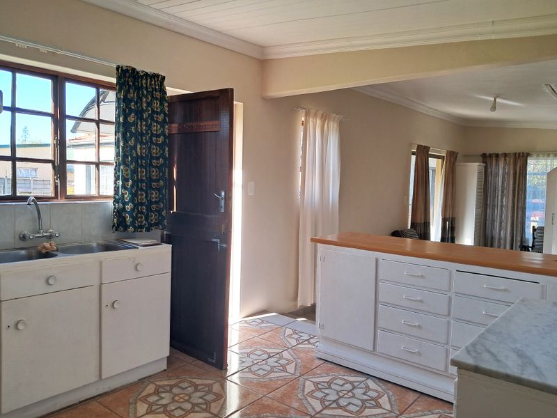 Open plan kitchen and living area featuring tiled flooring, built-in cabinetry, and direct access to the exterior through a wooden door.