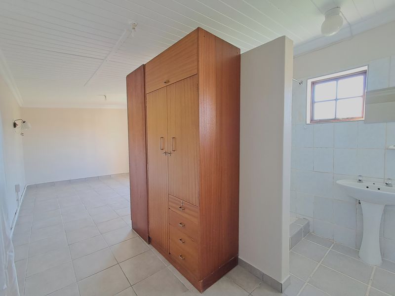 Spacious bedroom featuring a built-in wardrobe, tiled flooring, timber ceiling, and an open-plan en-suite area with a pedestal basin.