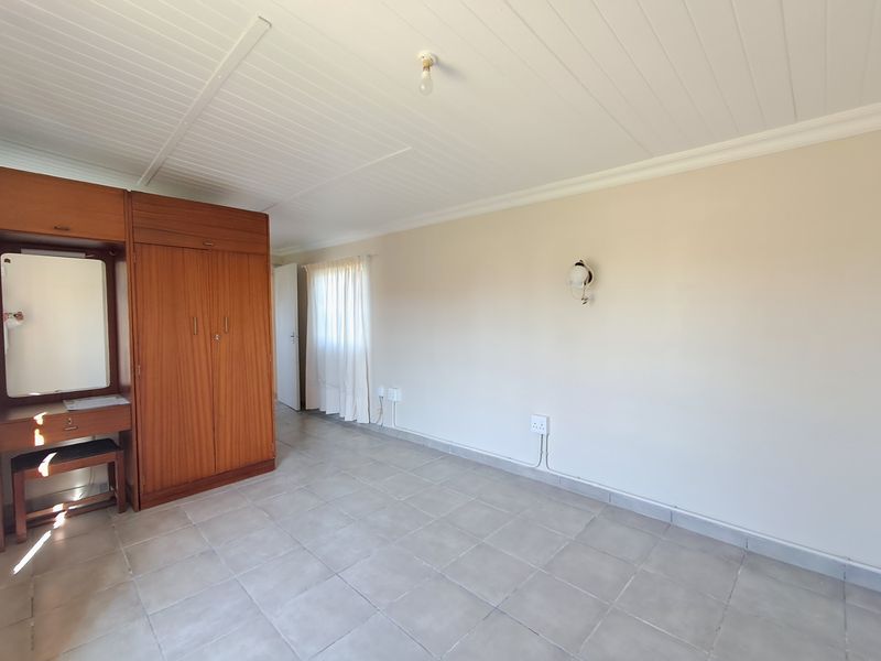 A bedroom featuring tiled flooring, a tongue and groove ceiling, and a built-in wooden wardrobe with an integrated vanity mirror.