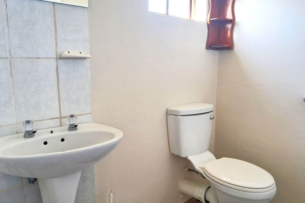 A functional bathroom featuring a pedestal washbasin and a standard toilet with tiled splashback and wall-mounted mirror.