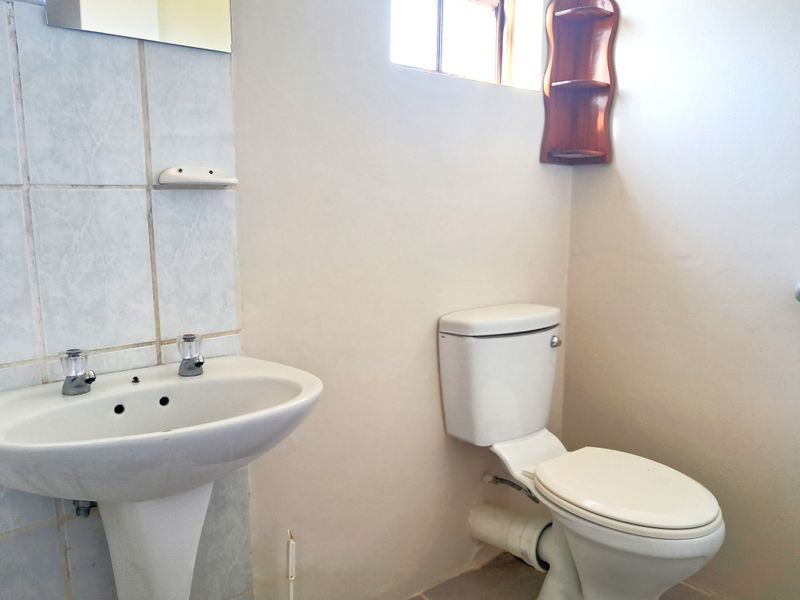 A functional bathroom featuring a pedestal washbasin and a standard toilet with tiled splashback and wall-mounted mirror.