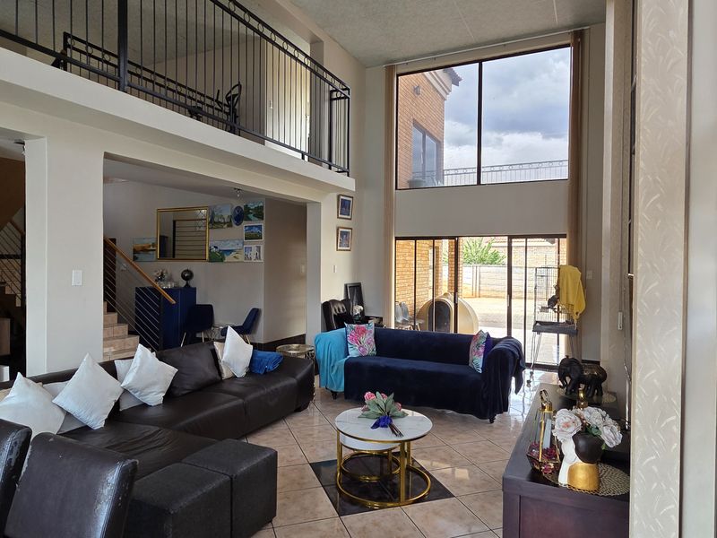 Spacious open-plan living area featuring double volume ceilings, a mezzanine level with wrought iron balustrades, and large windows providing abundant natural light.