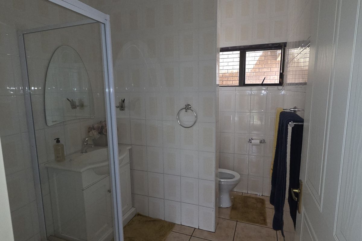 A functional bathroom featuring a shower enclosure, vanity basin, and a separate toilet area with tiled finishes throughout.