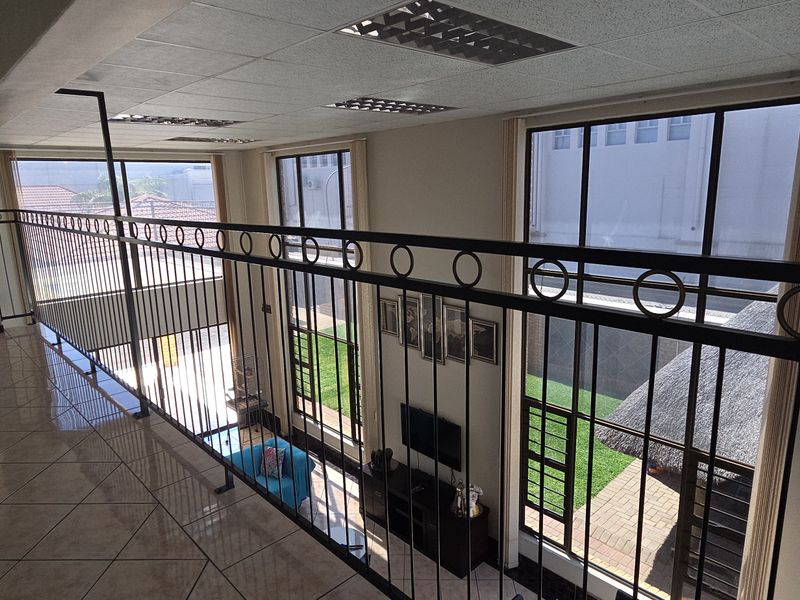 An elevated hallway featuring tiled flooring and a wrought iron balustrade, overlooking the lower level through large windows.
