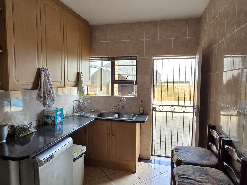 A functional scullery area featuring built-in wooden cabinetry, tiled wall finishes, and a stainless steel sink with direct access to the exterior.