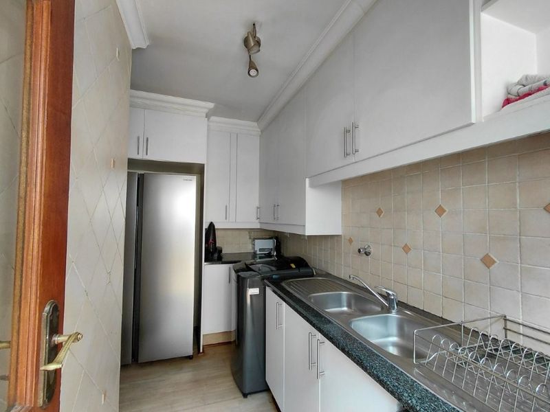 A functional scullery featuring white built-in cabinetry, granite countertops, and a double stainless steel sink with tiled backsplash.