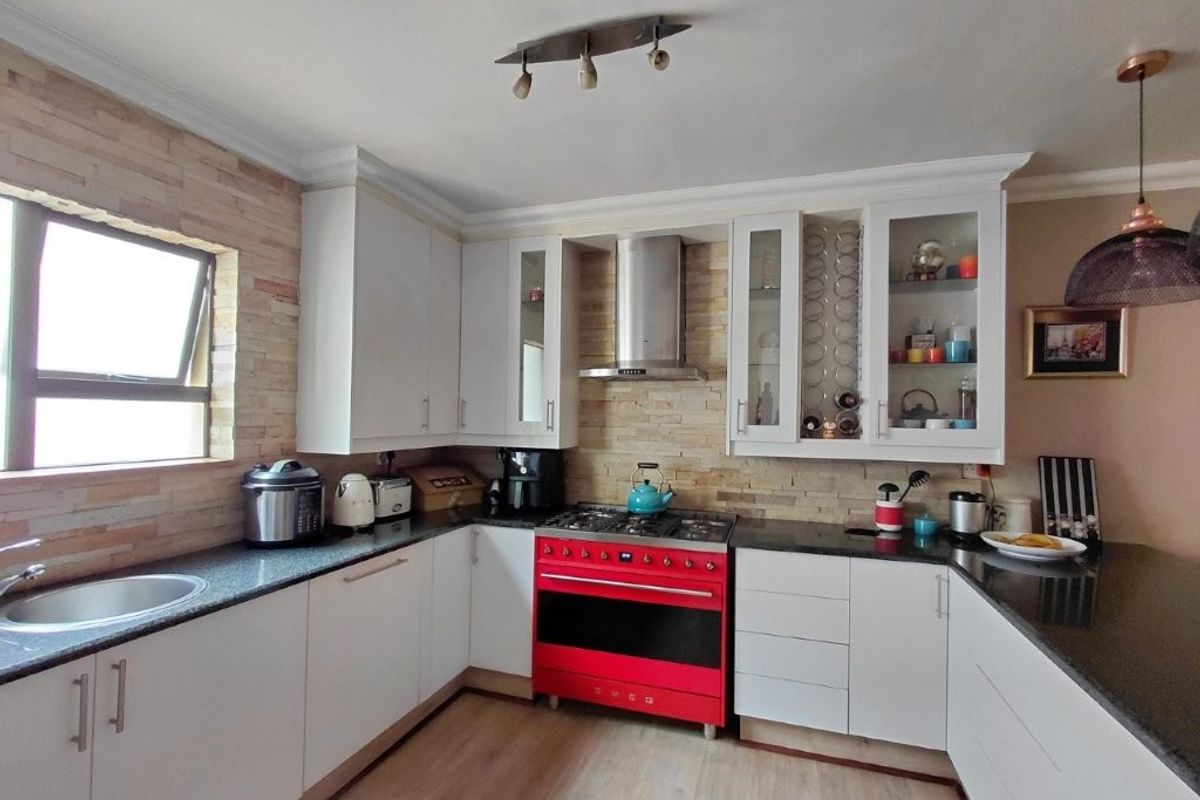 A well-appointed kitchen featuring white cabinetry, granite countertops, a stone-clad backsplash, and a prominent red gas stove with a stainless steel extractor fan.