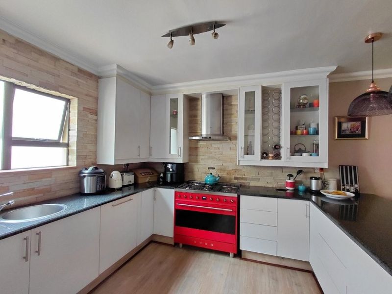 A well-appointed kitchen featuring white cabinetry, granite countertops, a stone-clad backsplash, and a prominent red gas stove with a stainless steel extractor fan.