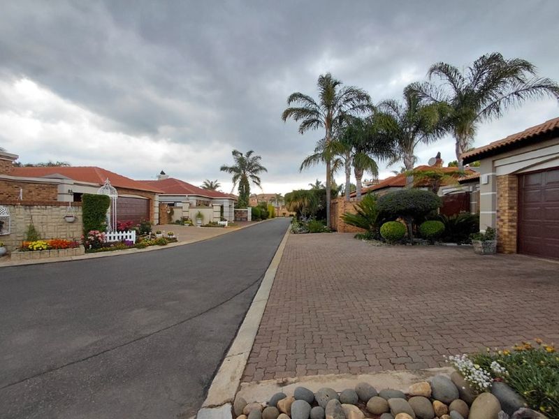 A view of a residential street featuring paved driveways, brick-faced homes with tiled roofs, and established landscaping.