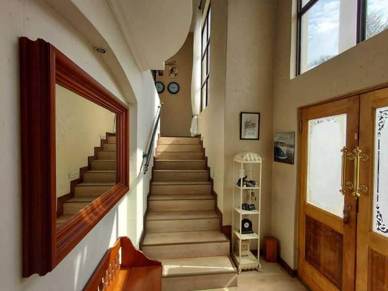 Welcoming entrance foyer featuring a timber staircase, double-height ceilings, and natural light, creating an open and airy atmosphere.
