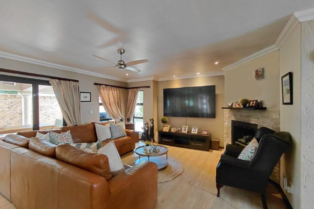 A comfortable living room featuring a stone-surround fireplace, ceiling fan, recessed lighting, and sliding glass doors leading to the outdoor area.