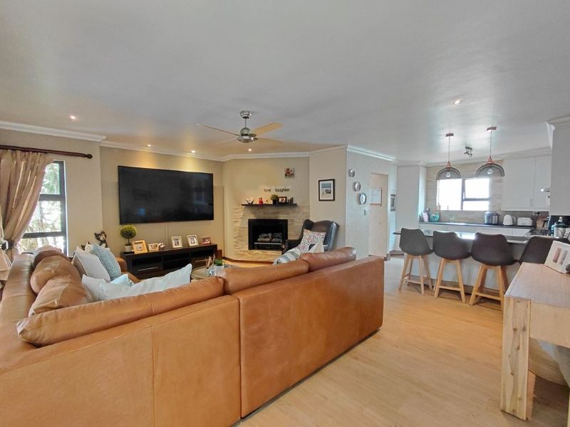 Spacious open-plan living area featuring a stone-clad fireplace, modern kitchen with island seating, and light wood-look flooring throughout.