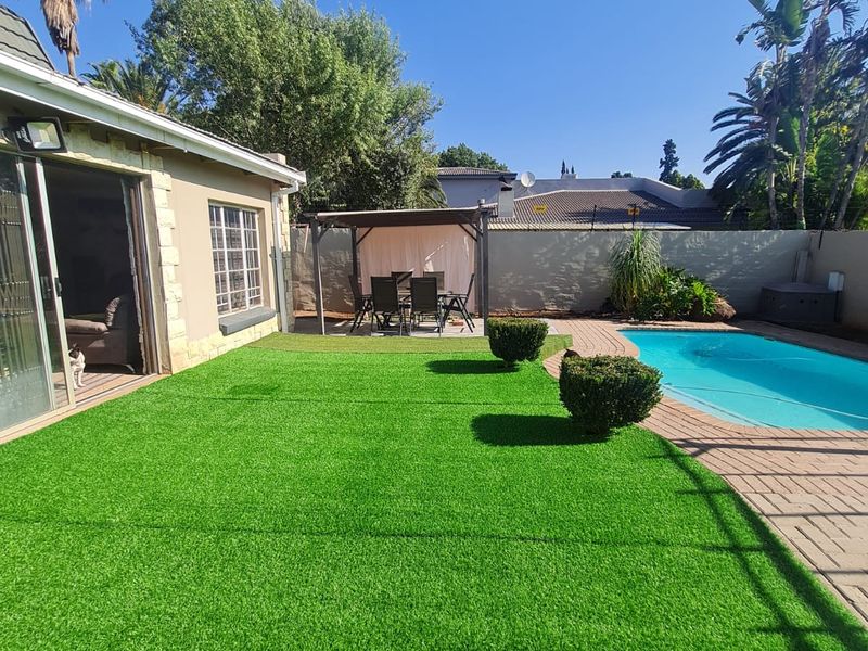 A well-maintained rear garden featuring an artificial lawn, a swimming pool with paved surround, and a covered patio area.