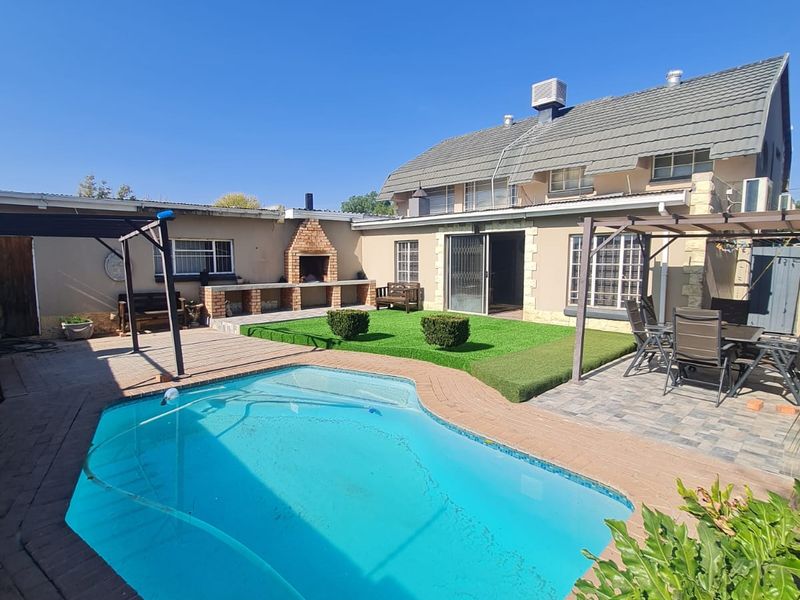 Outdoor entertainment area featuring a swimming pool, paved patio, built-in braai, and artificial lawn, perfect for hosting and relaxation.