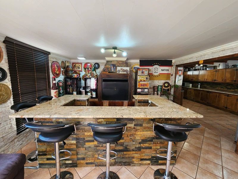 A dedicated entertainment bar area featuring a stone-clad built-in bar with granite countertop, integrated indoor braai, and tiled flooring.