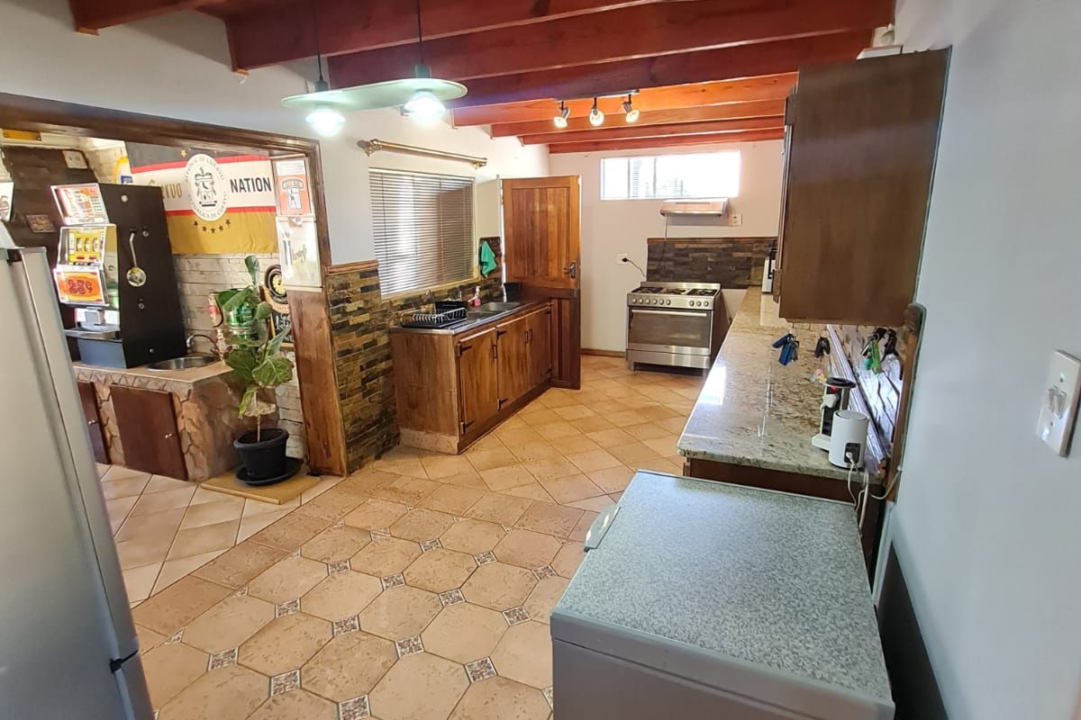 Spacious kitchen featuring exposed timber ceiling beams, granite countertops, wooden cabinetry, and a freestanding gas stove with tiled flooring throughout.