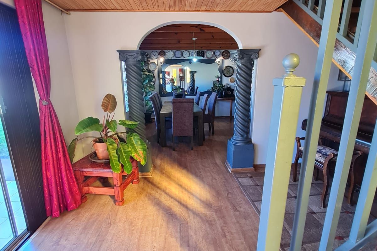 Living area featuring a timber ceiling, decorative columns, and an archway leading to the dining room, with a staircase and sliding door access.