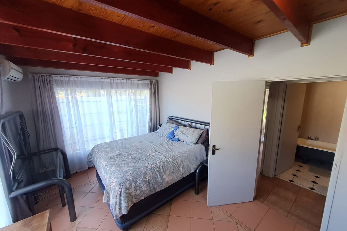 Bedroom featuring exposed timber ceiling beams, tiled flooring, and an en-suite bathroom, offering a functional layout with potential for cosmetic updates.