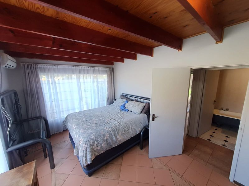 Bedroom featuring exposed timber ceiling beams, tiled flooring, and an en-suite bathroom, offering a functional layout with potential for cosmetic updates.