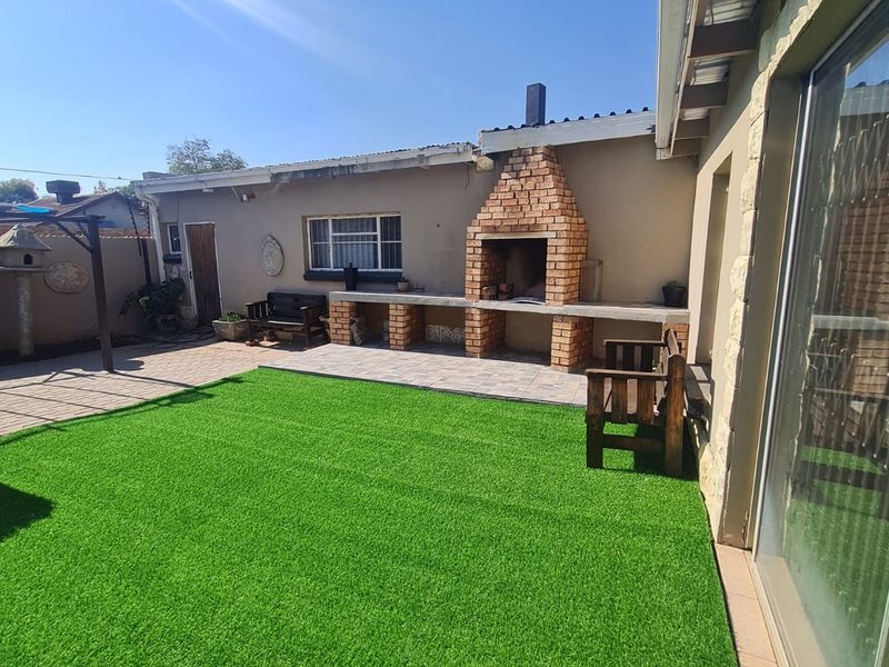 Outdoor patio area featuring a built-in brick braai, concrete prep surface, and artificial lawn, providing a functional space for outdoor entertaining.