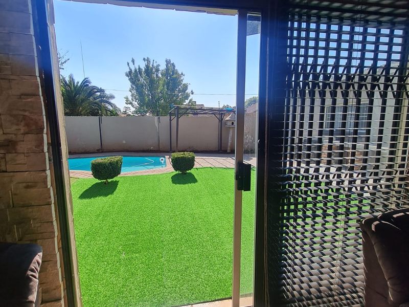 View from an interior space through a sliding door onto a private backyard featuring a swimming pool, artificial lawn, and perimeter wall.