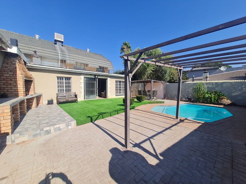 Rear garden featuring a swimming pool, paved patio area, pergola, and a built-in brick braai, perfect for outdoor entertaining.