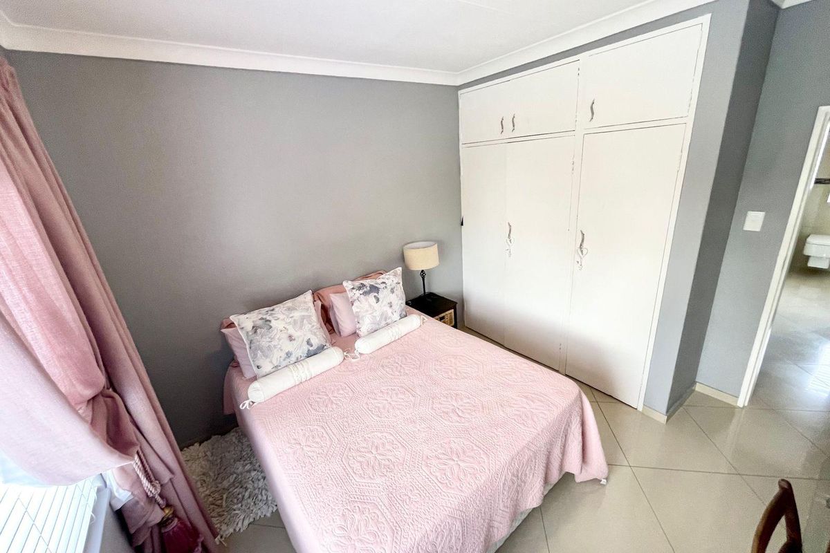 A bedroom featuring built-in floor-to-ceiling cupboards, tiled flooring, and neutral grey wall tones.
