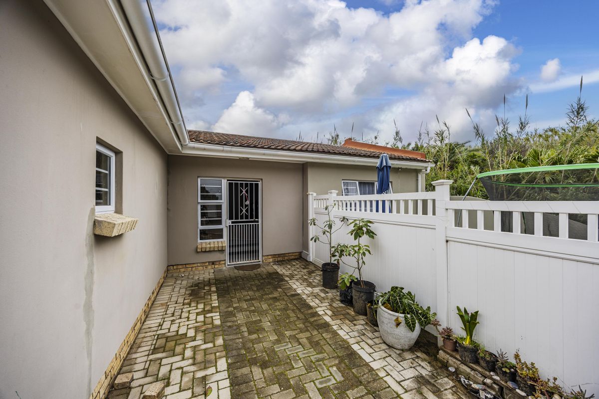 A rear exterior view of the townhouse featuring a paved walkway, security gate, and white vinyl fencing along the perimeter.