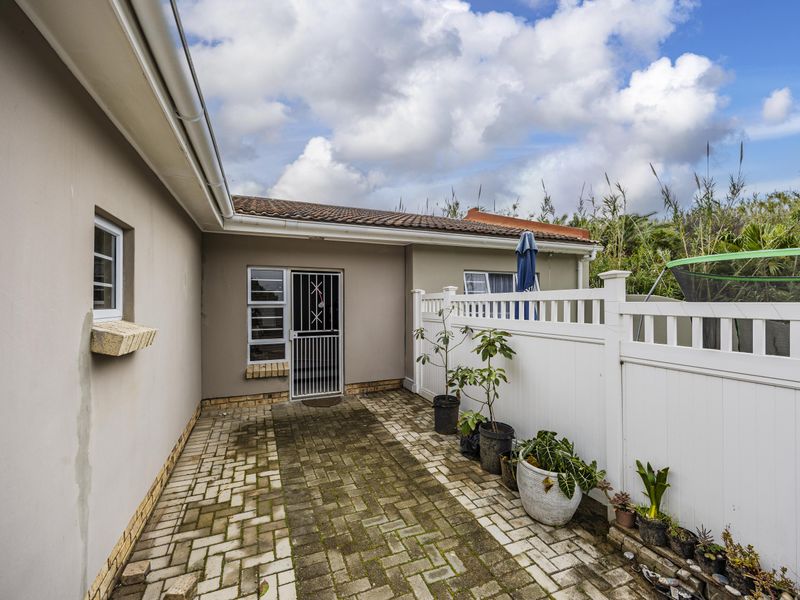 A rear exterior view of the townhouse featuring a paved walkway, security gate, and white vinyl fencing along the perimeter.