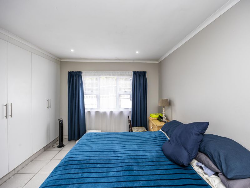 A well-maintained bedroom featuring neutral walls, tiled flooring, recessed downlights, and ample built-in cupboard storage.