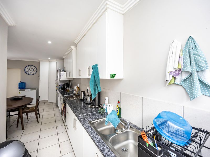 A functional galley-style kitchen featuring white cabinetry, dark laminate countertops, a stainless steel double sink, and tiled flooring.
