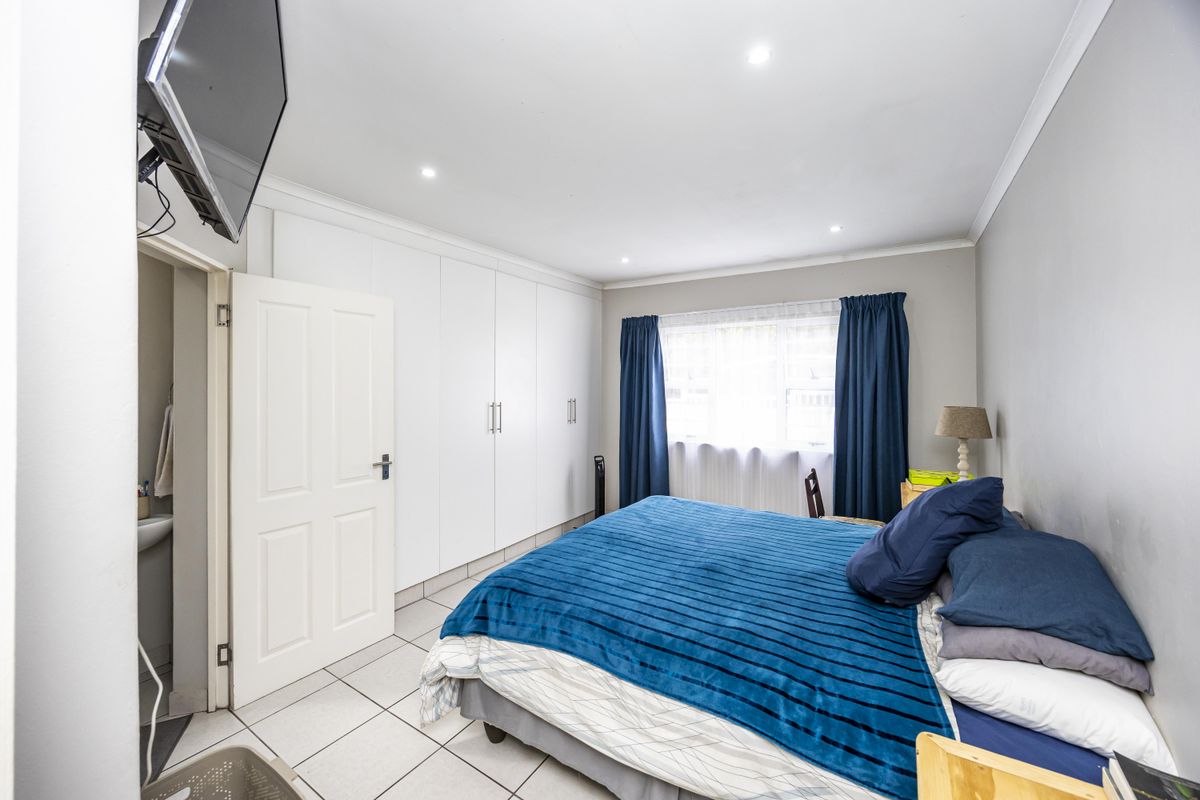 A well-lit bedroom featuring built-in cupboards, tiled flooring, and an en-suite bathroom, offering a clean and functional living space.