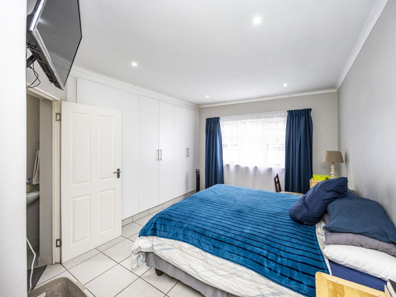 A well-lit bedroom featuring built-in cupboards, tiled flooring, and an en-suite bathroom, offering a clean and functional living space.