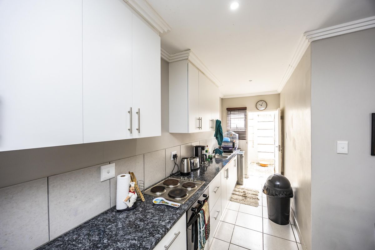 A functional galley-style kitchen featuring white cabinetry, granite countertops, an integrated electric hob and oven, and direct access to an outdoor area.
