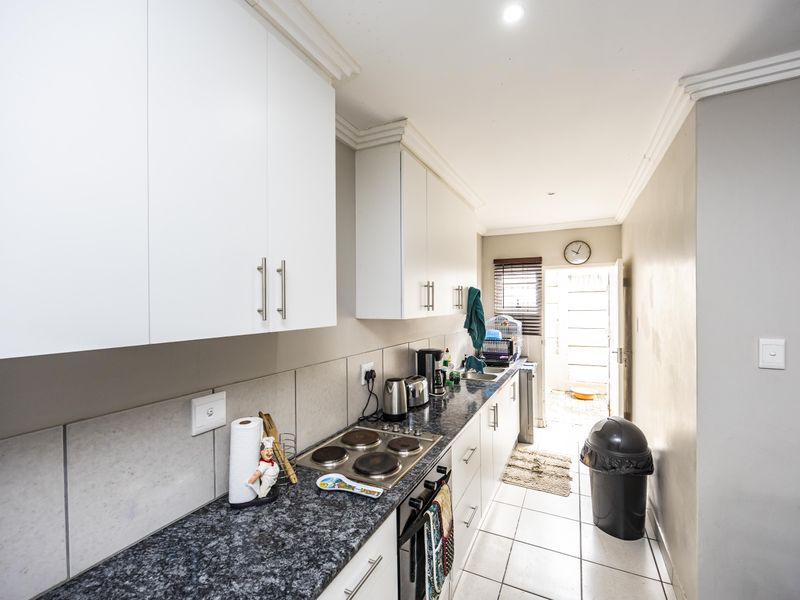 A functional galley-style kitchen featuring white cabinetry, granite countertops, an integrated electric hob and oven, and direct access to an outdoor area.
