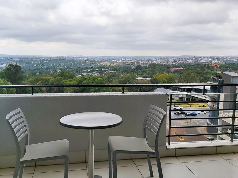 A balcony featuring tiled flooring and a metal balustrade, offering an expansive elevated view of the surrounding urban landscape.