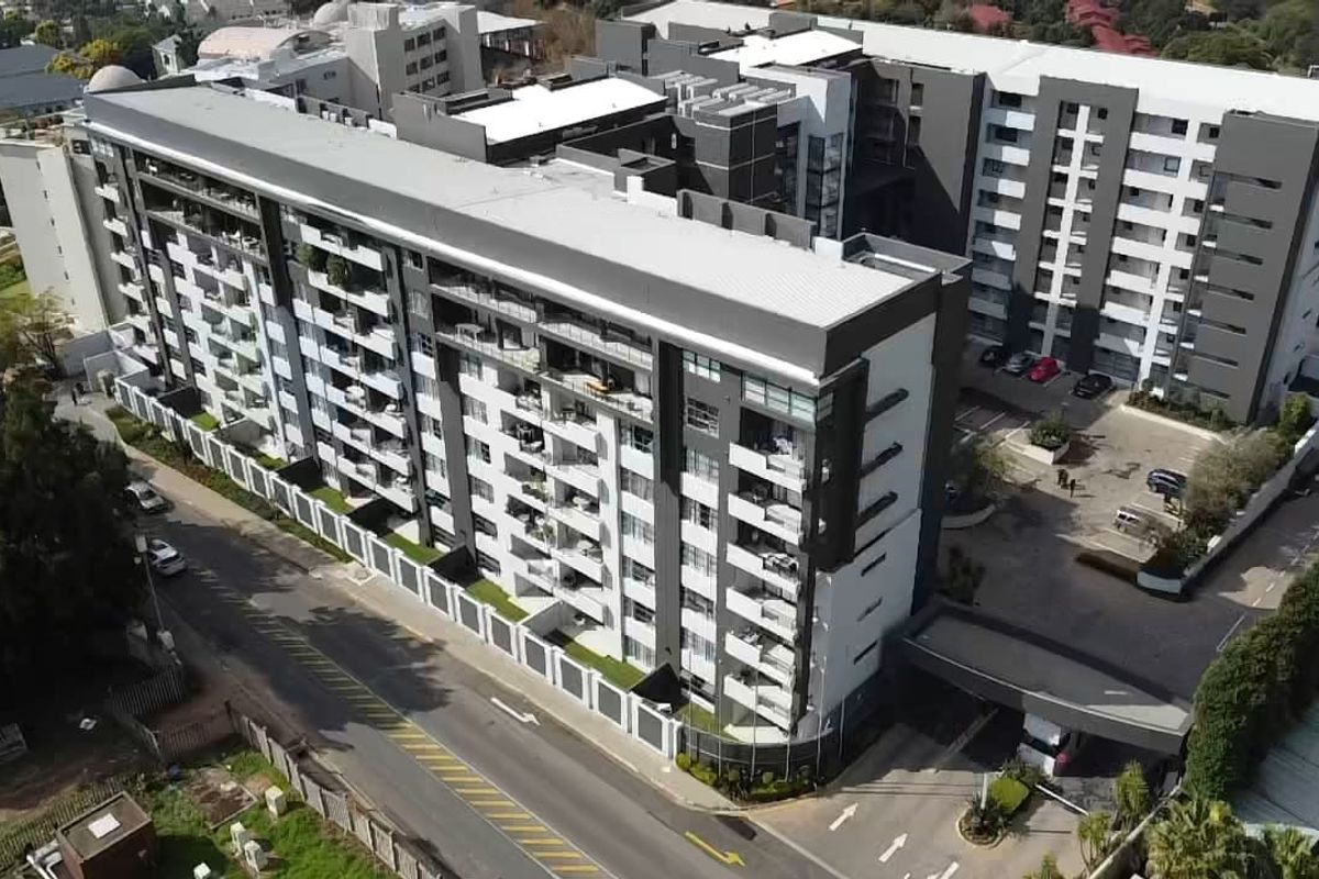 Aerial view of a modern multi-story apartment complex featuring balconies, secure parking, and a gated entrance.