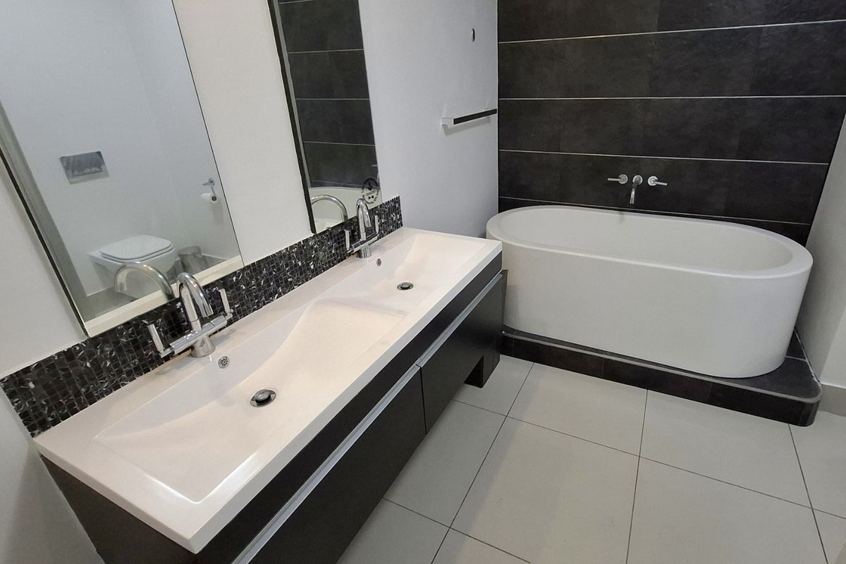 Modern bathroom featuring a double vanity with mosaic splashback, a sleek freestanding bathtub, and contemporary wall-mounted fixtures.