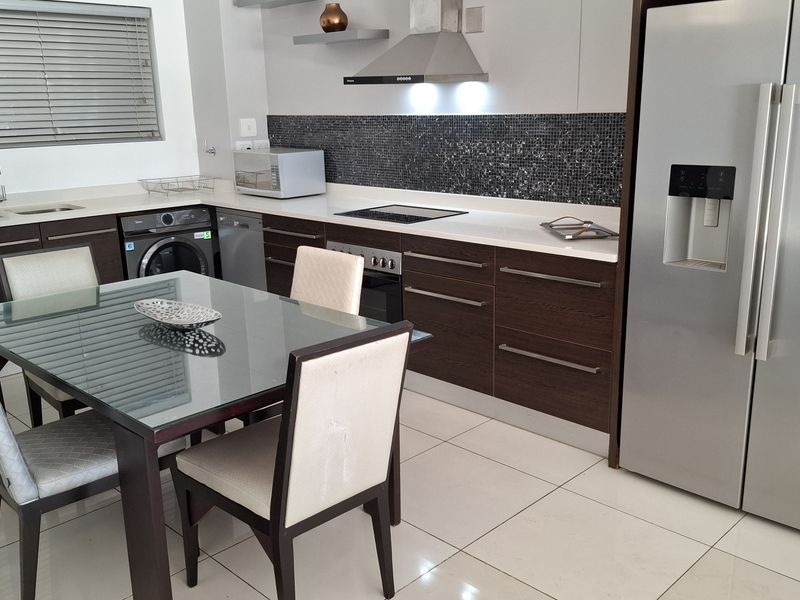 Modern open-plan kitchen featuring dark wood cabinetry, stone countertops, mosaic backsplash, and integrated stainless steel appliances, seamlessly flowing into the dining area.