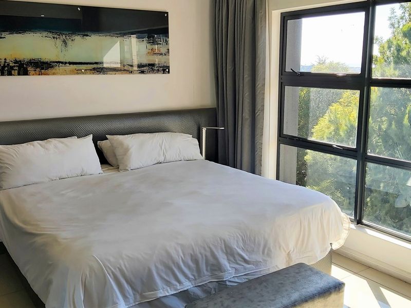 A well-lit bedroom featuring large windows that provide natural light and views of the surrounding greenery.
