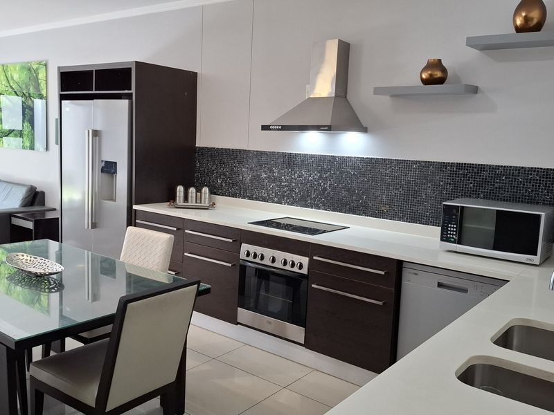 Modern open-plan kitchen featuring dark cabinetry, mosaic backsplash, stainless steel appliances, and a seamless transition to the dining area.