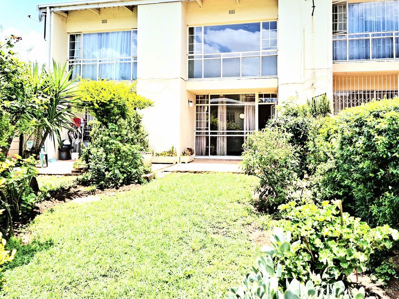 Rear view of the apartment building featuring a private garden, paved patio area, and large windows with security bars.