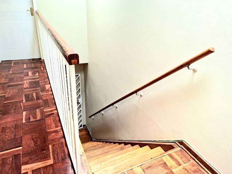 A hallway featuring parquet flooring, a wooden handrail, and a metal balustrade leading down a staircase with a security gate.