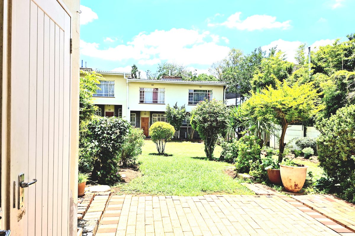 A view of a rear garden featuring a paved patio area and established landscaping, looking towards the back facade of the apartment building.