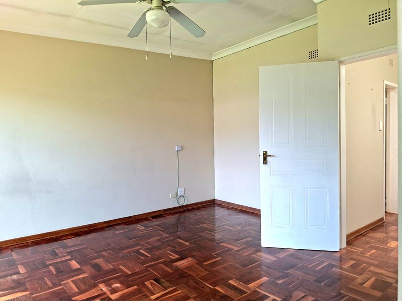 An empty bedroom featuring classic parquet flooring, a ceiling fan, and neutral wall finishes, offering a blank canvas for personalization.
