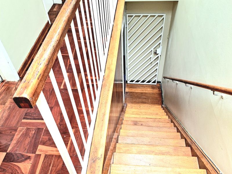 A staircase featuring wooden parquet flooring, a metal balustrade with a wooden handrail, and a security gate at the base.