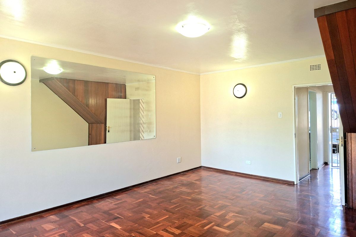 Spacious living area featuring classic parquet flooring, a large wall-mounted mirror, and timber staircase detailing, offering a blank canvas for interior design.